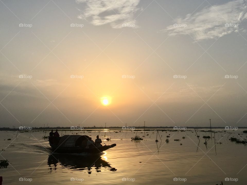 A boat’s silhouette reflects the orange rays of the sun as it passes through the Meghna River