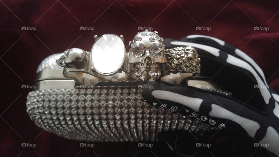 A skeleton glove holding a hand purse with skulls and jewels