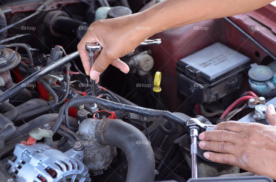 A man is working hard with engine repairs using a variety of tools as he attempts to install a new alternator.