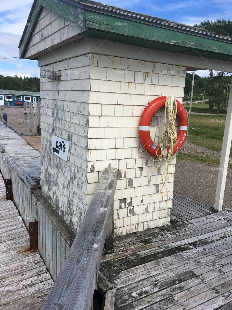 Weathered Seaside building on wharf. Painted sign pointing to cafe. Life saving buoy and rope hanging. Marine, nautical scene. 