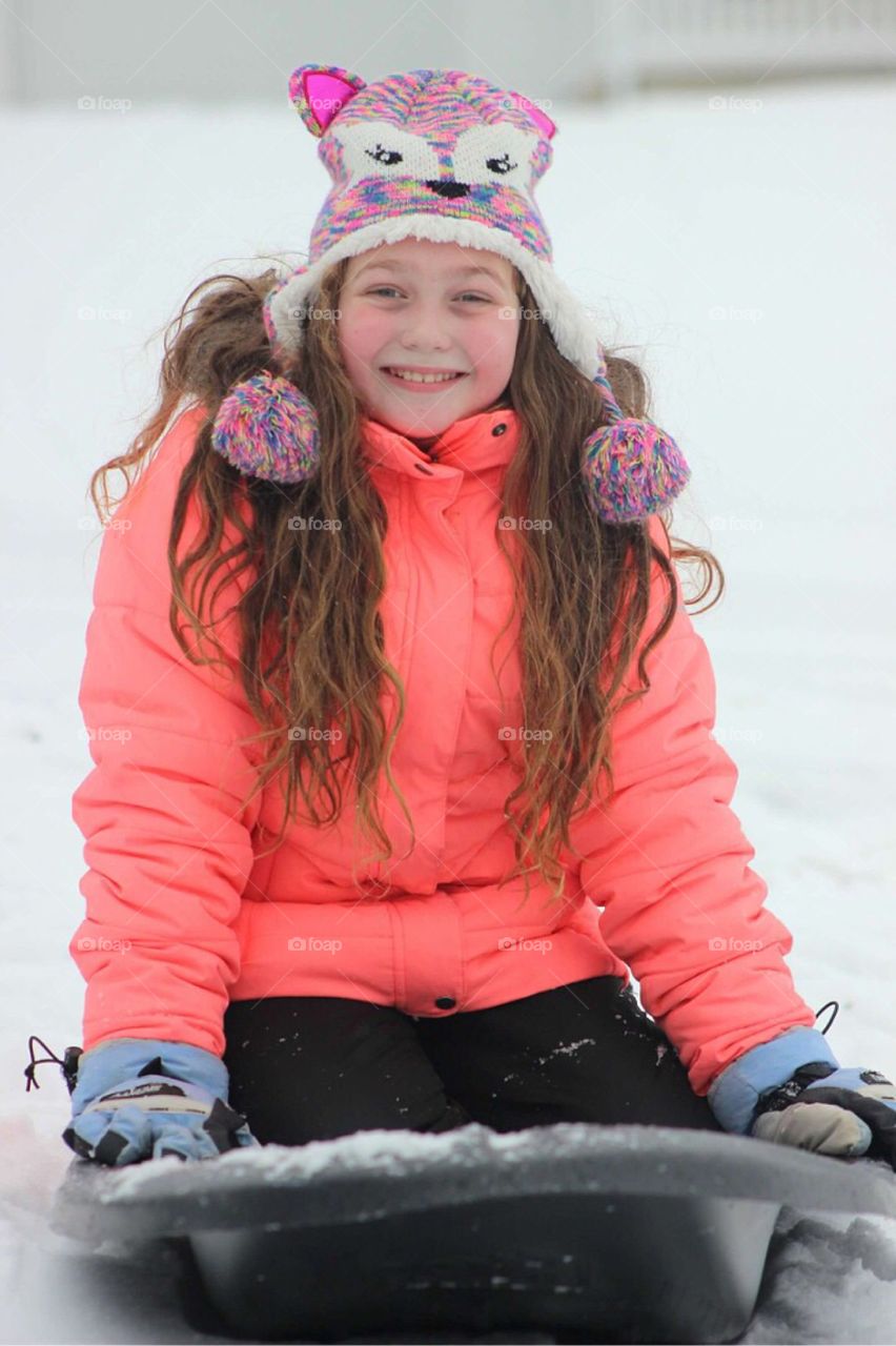Smiling girl sitting on sled during winter