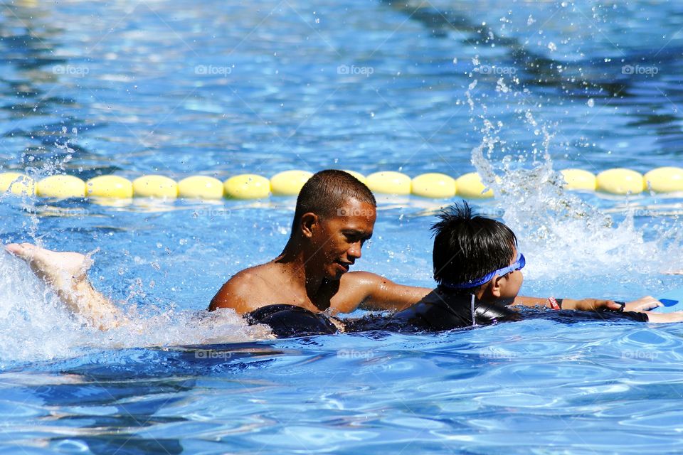 young kid learns how to swim with the help of a swimming coach