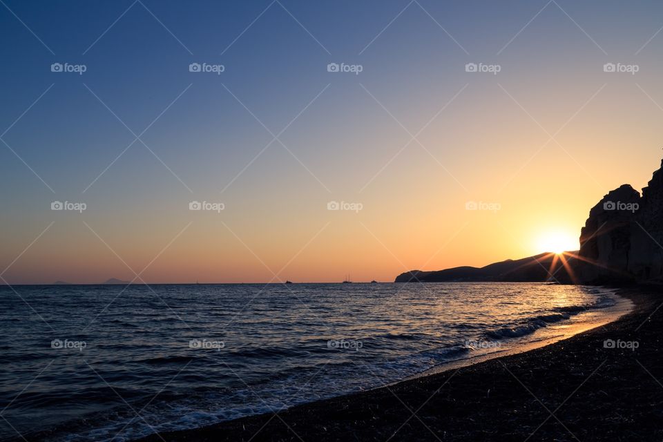 Vlychada beach in Santorini. The sun is setting behind a rock at the beautiful Vlychada beach in Santorini, Greece.
