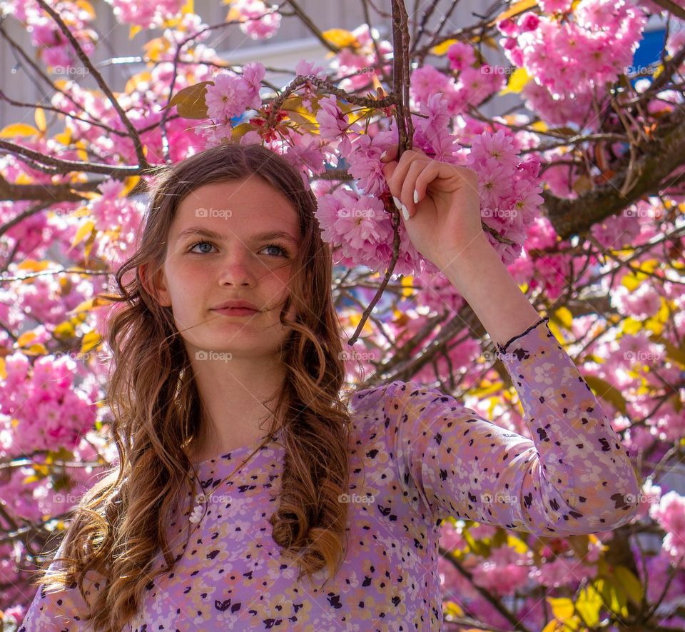 Beautiful teen girl standing under a Apple tree in full colorfull blooming. 
Pink its all over and very Beautiful