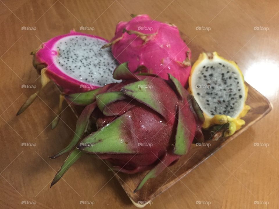 Yellow, pink, red dragon fruits cut in half on wooden plate