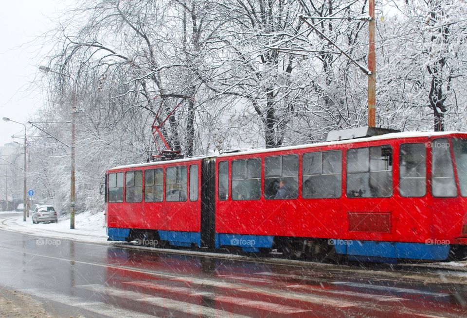 Winter landscape in the city.  While the snow is falling and old red tram slides down the street