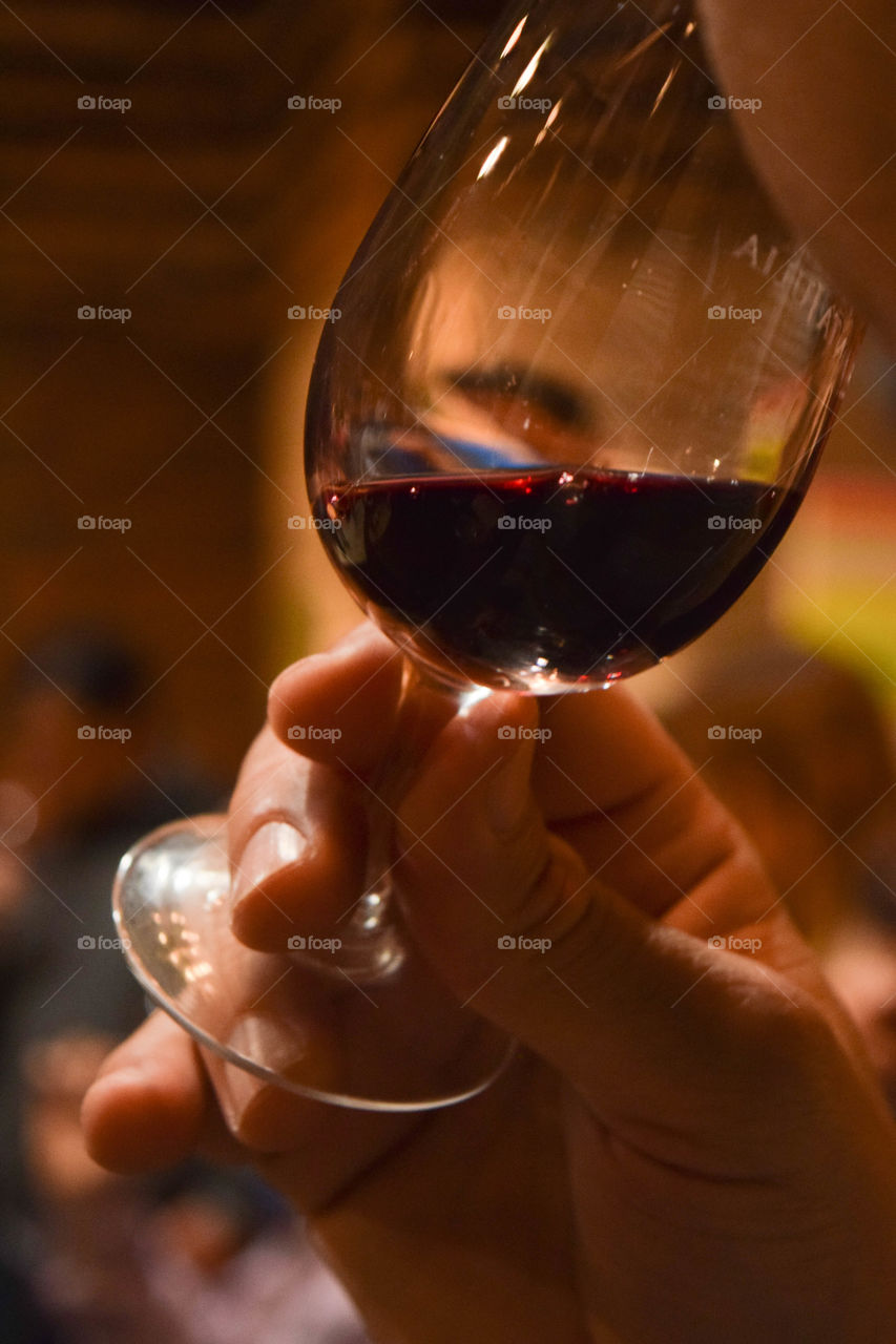 Mão masculina levando à boca uma taça de vinho tinto.
