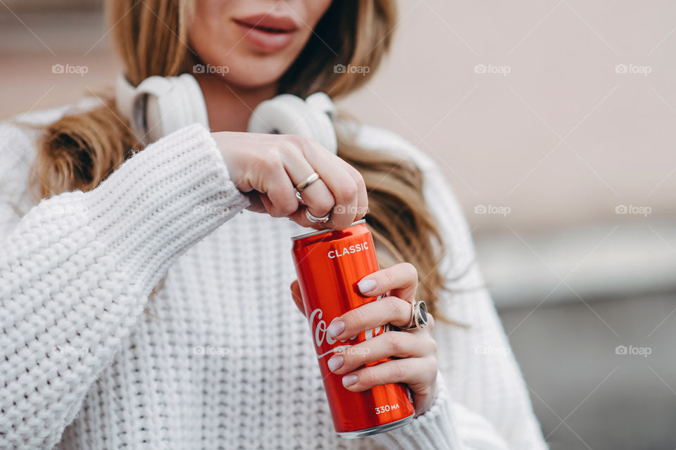 A woman in white sweater opens Coca-Cola red can