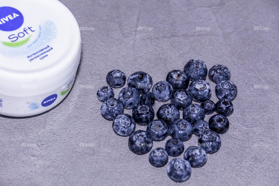 Cosmetic Nivea skin care product on a gray surface with a fresh, fragrant blueberry lined with a heart.