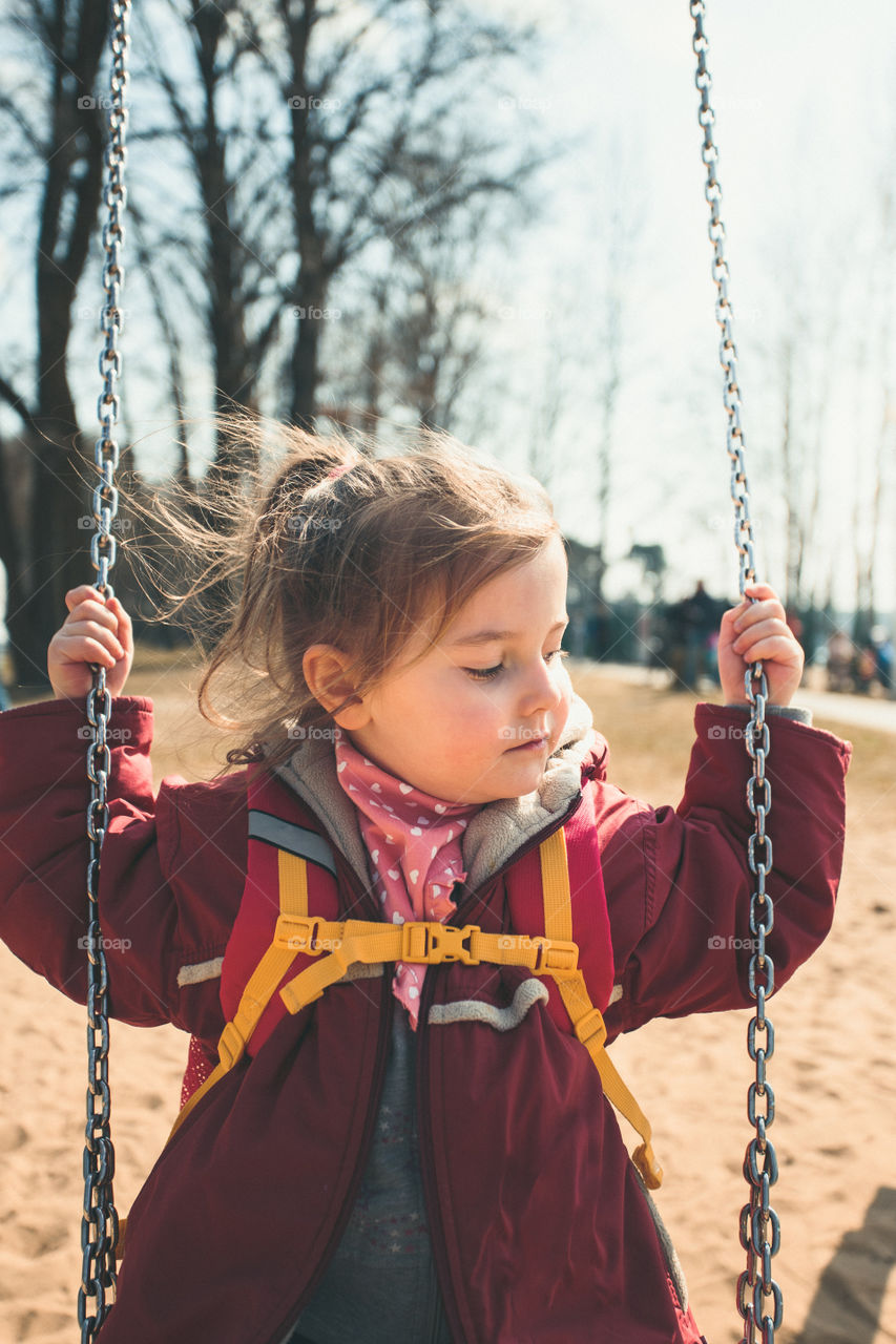 Little cute girl swinging in a park on sunny spring day. Child wearing red jacket