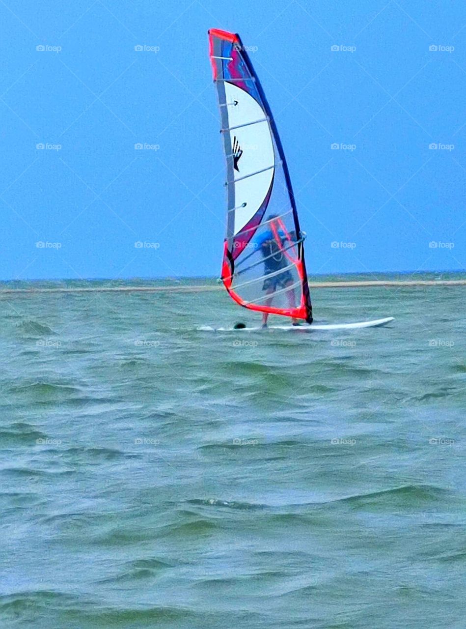 A man controls a sail on a surfboard in the sea against the background of water and sky. Movement on water
