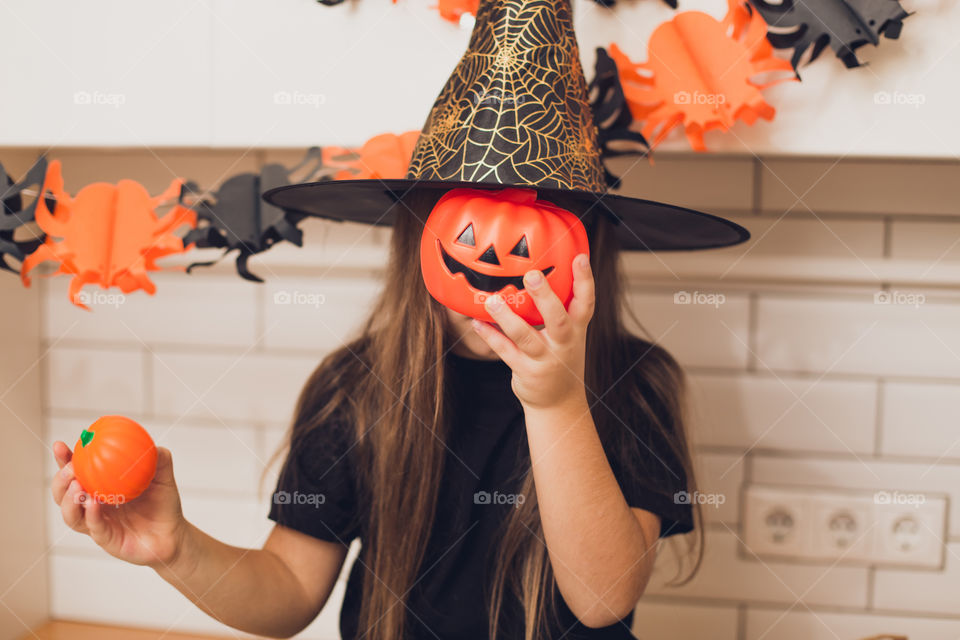 Little girl dressed as a witch for halloween holding a pumpkin with a face on the background decor