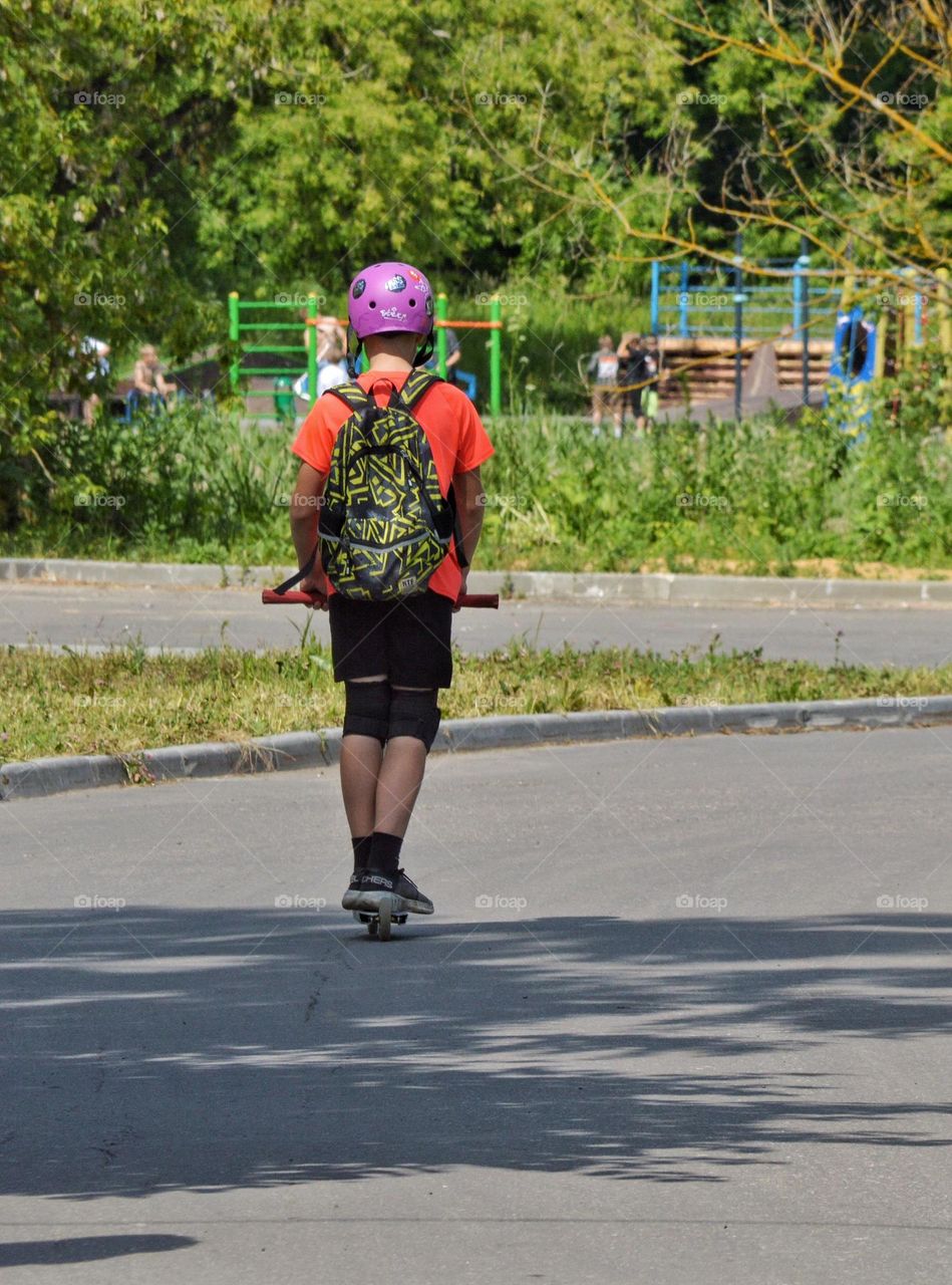 a boy in a lilac helmet rides a scooter