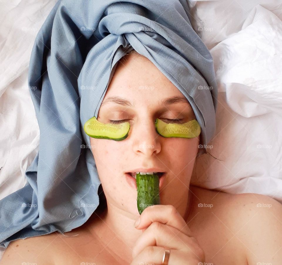 portrait of a white-skinned girl during home cosmetic procedures, namely a homemade cucumber mask in a blue towel