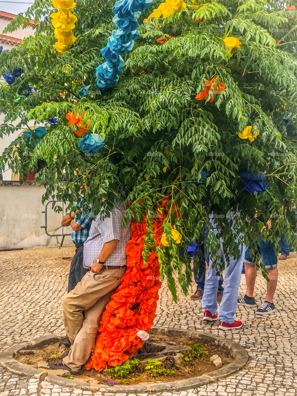 People are obscured from view as they shade under tree, decorated with bright colours for a Portuguese Festa 