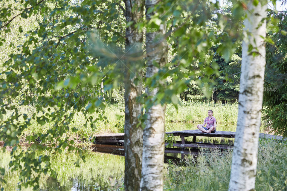 Woman sitting on a bridge over a lake, among the trees, close to nature, during summer vacations. Candid people, real moments, authentic situations