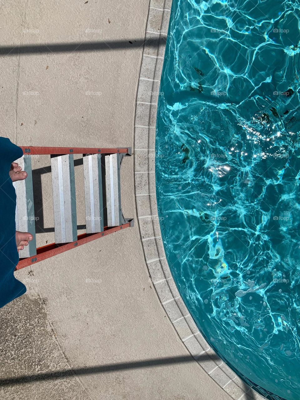 Child about to jump in inground pool deep end to swim from the ladder, seen from the child perspective on high stairs with blue crystal looking water.