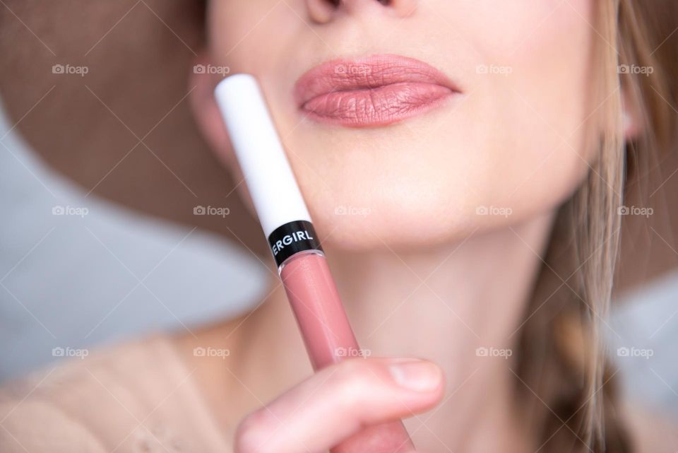 Closeup of a woman holding a tube of lip color to her face 