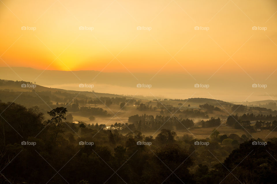 Sunrise over the valleys and mountains with fog rising from the water. Golden sunrise with trees and lakes.