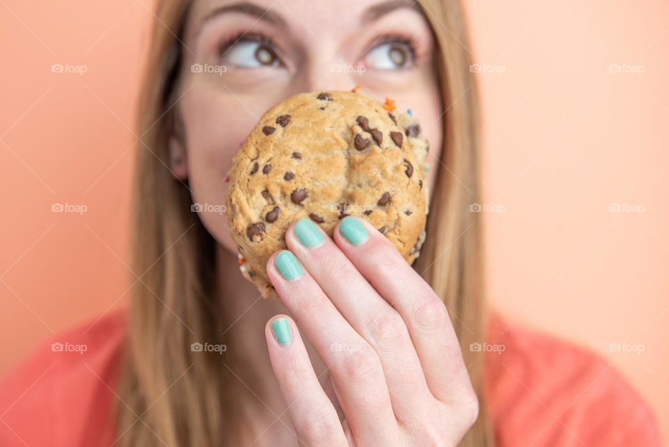 Woman with painted nails holding a chocolate chip cookie in front of her face 