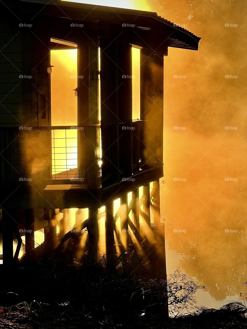 Silhouette of boathouse on a calm lake, backlit by the sunrise and mist creating an orange glow.