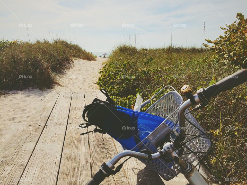 Bike with snorkeling gear in basket at the beach. Bicycle handle bars pointed at Gulf of Mexico with fins for snorkeling in a basket, surrounded by sand and sea grass at picnic table.