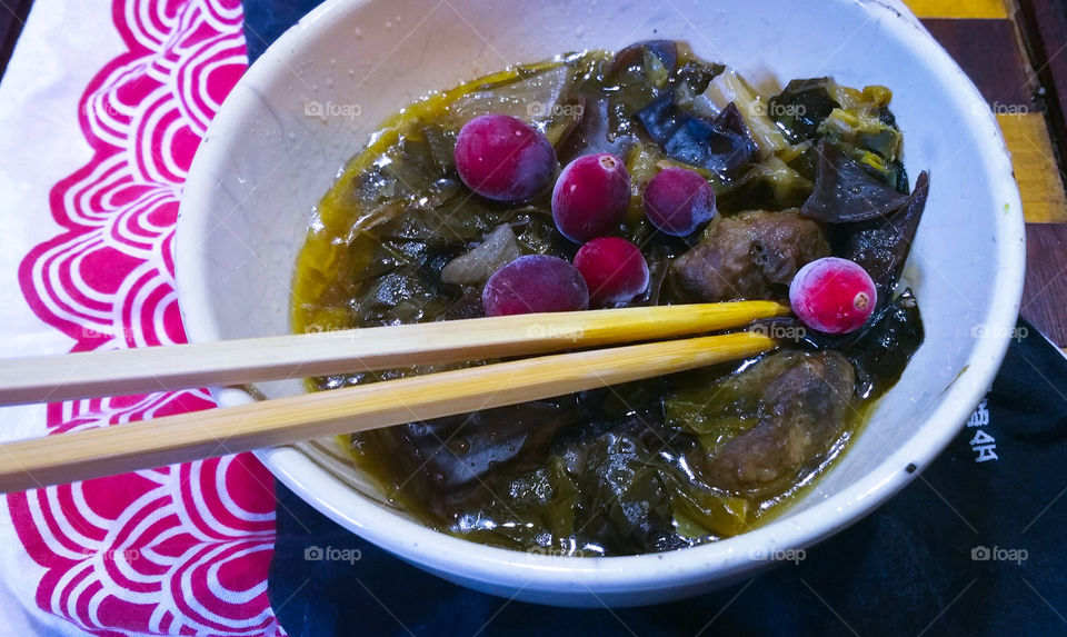 A bowl of food with red berries and chopsticks