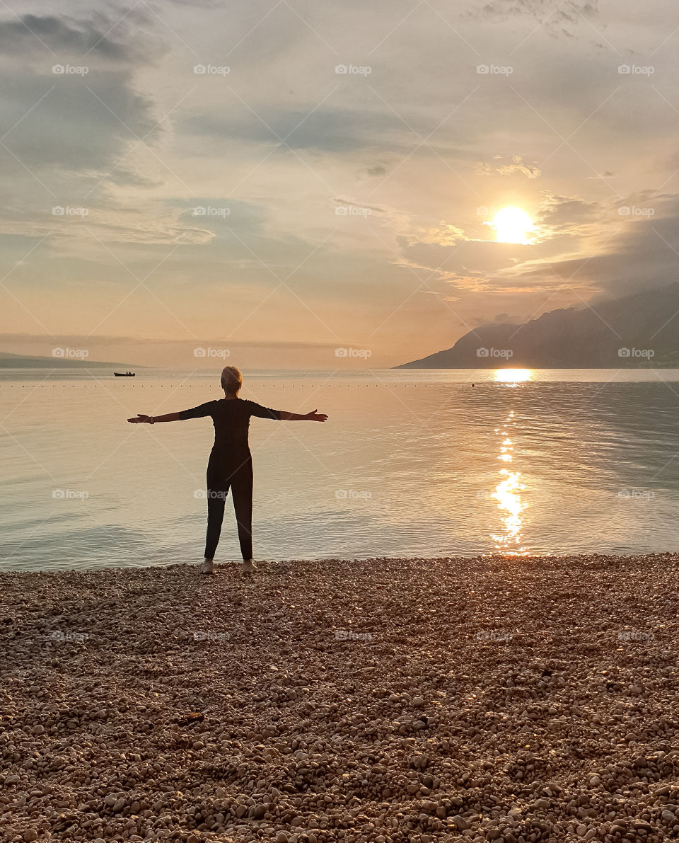 Silhouette of a slender woman looking at the sunset, which stands on the seashore.  Enjoying a relaxing summer vacation