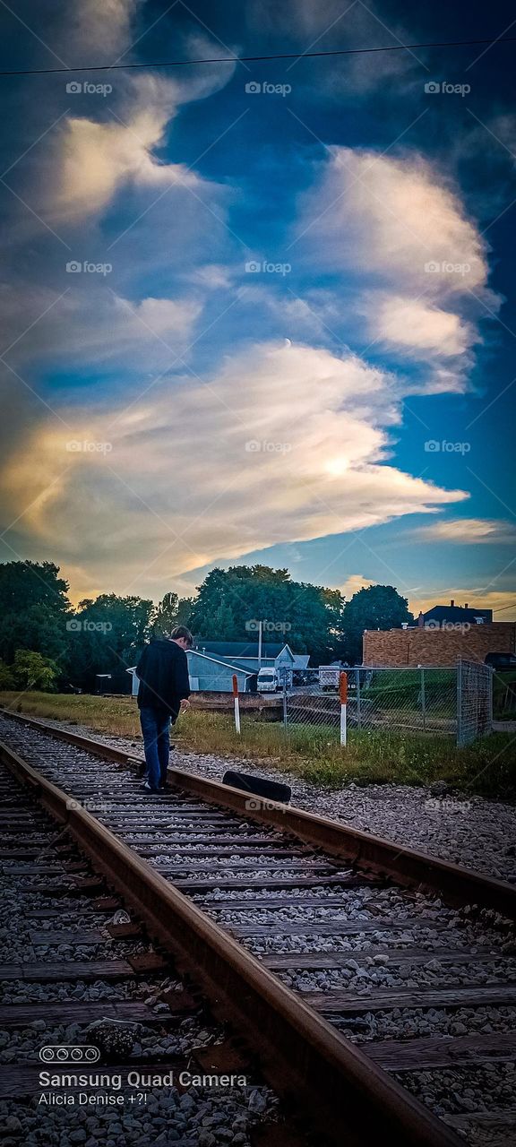 This is a picture of a young man walking in the railroad tracks in a small town the sky behind is absolutely breathtaking 