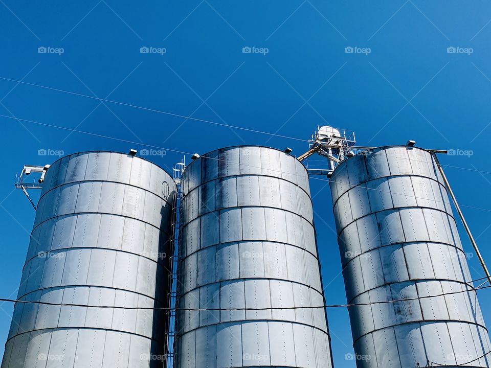 Silver metal silos against a bright blue sky