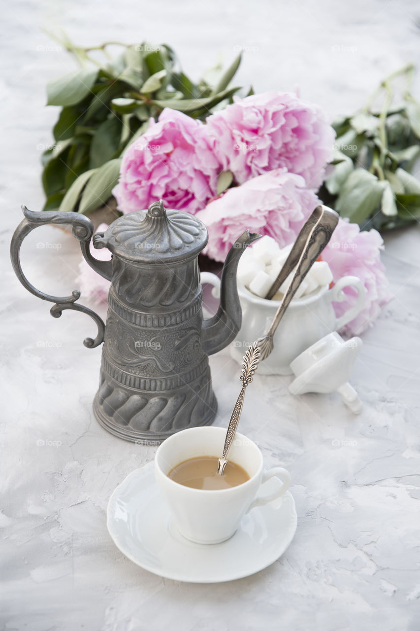 coffee with milk and sugar on a background of pink peonies on a light gray cement background