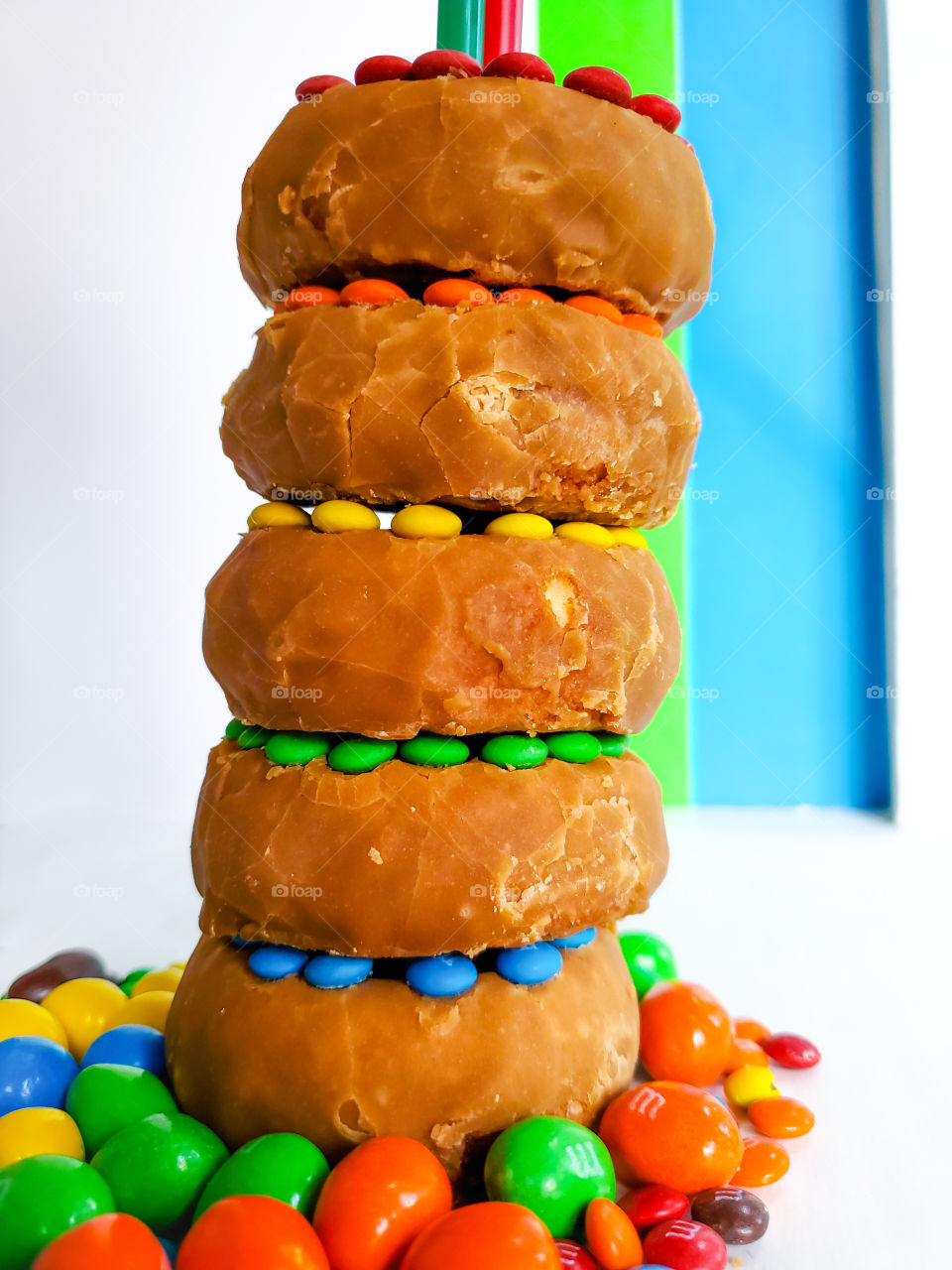 Stacked donuts decorated with M&M minis and surrounded by peanut M&Ms on a white surface with a blue, green and white solid background. Reminiscent of the classic Fisher Price rock-a- stack infant toy.