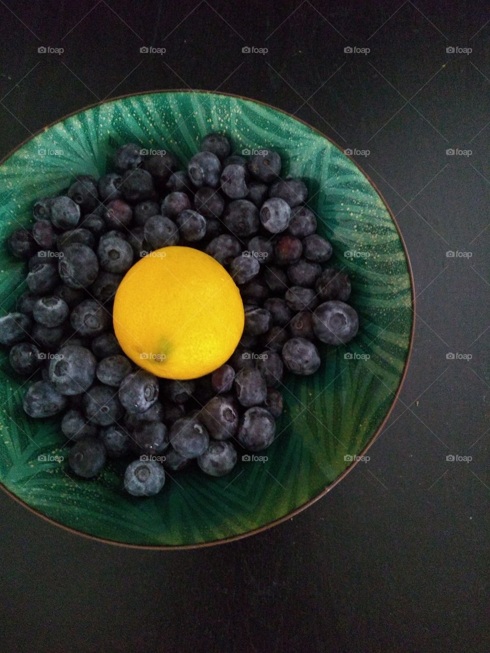 inside the bowl of this picture is blueberries and lemon done on a black table.