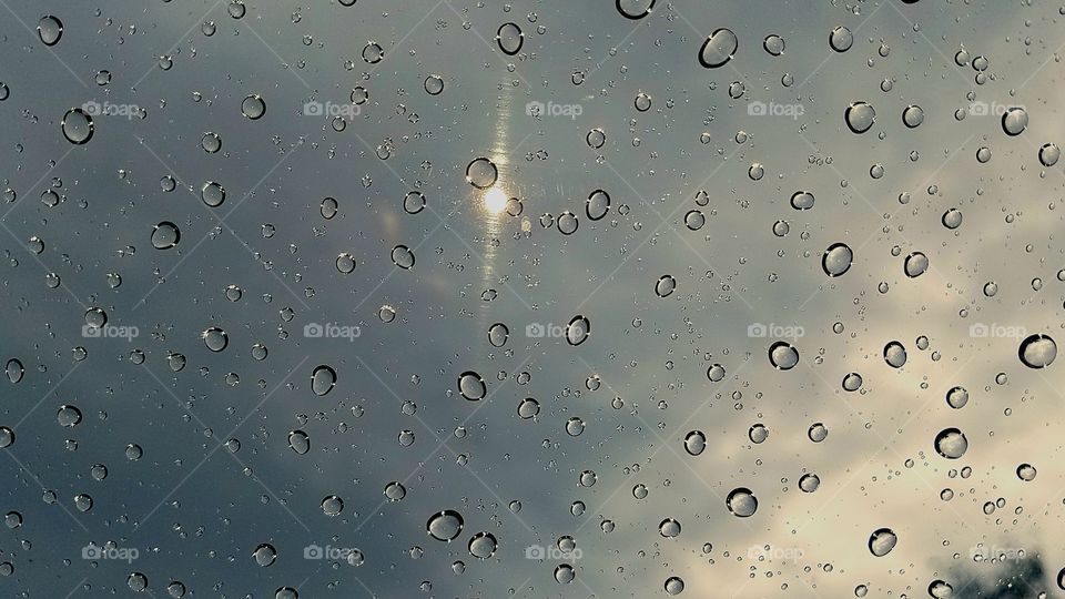 Raindrops on windshield of car with sky in background.