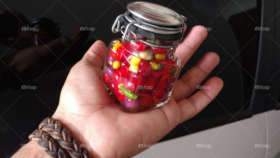 Frasco de vidro. Mão com pimentas frescas, coloridas.