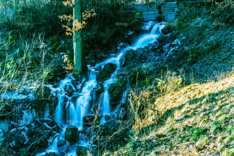 long exposure photo of a small waterfalls in the middle of the forest with good run off from the melting snow