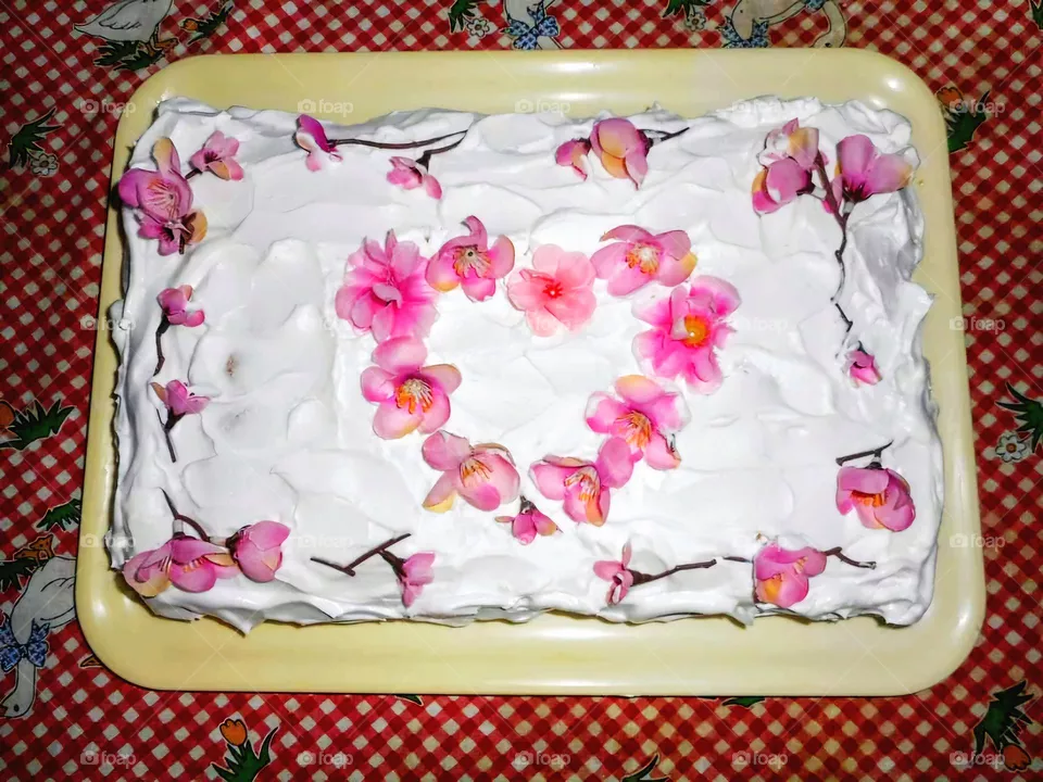Homemade milk cream cake with rose decorations forming a heart on a checkered tablecloth