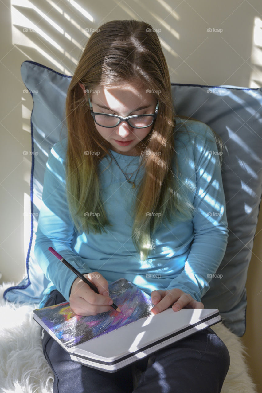 Girl sitting in a window seat drawing in a sketch pad