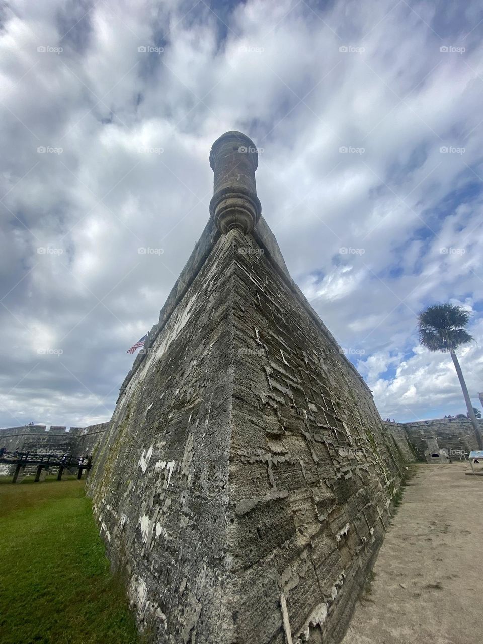 The corner of a coquina rock fortress against a blue sky with white clouds and palm tree beside it