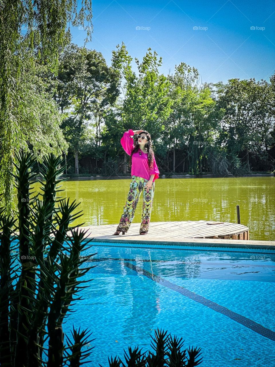 A girl with curly hair between a pool and a lake