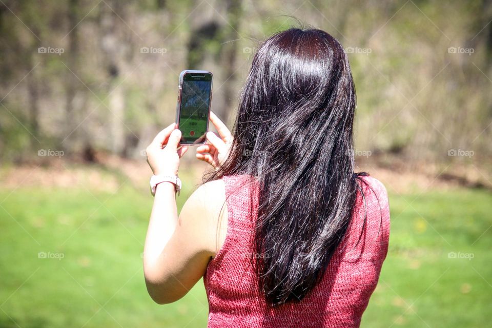 Woman with healthy long natural dark hair is taking a picture on her call phone outdoors