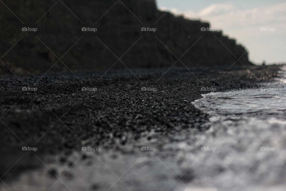 A beach of black volcanic pebbles under a cliff near a salt mineral lake
