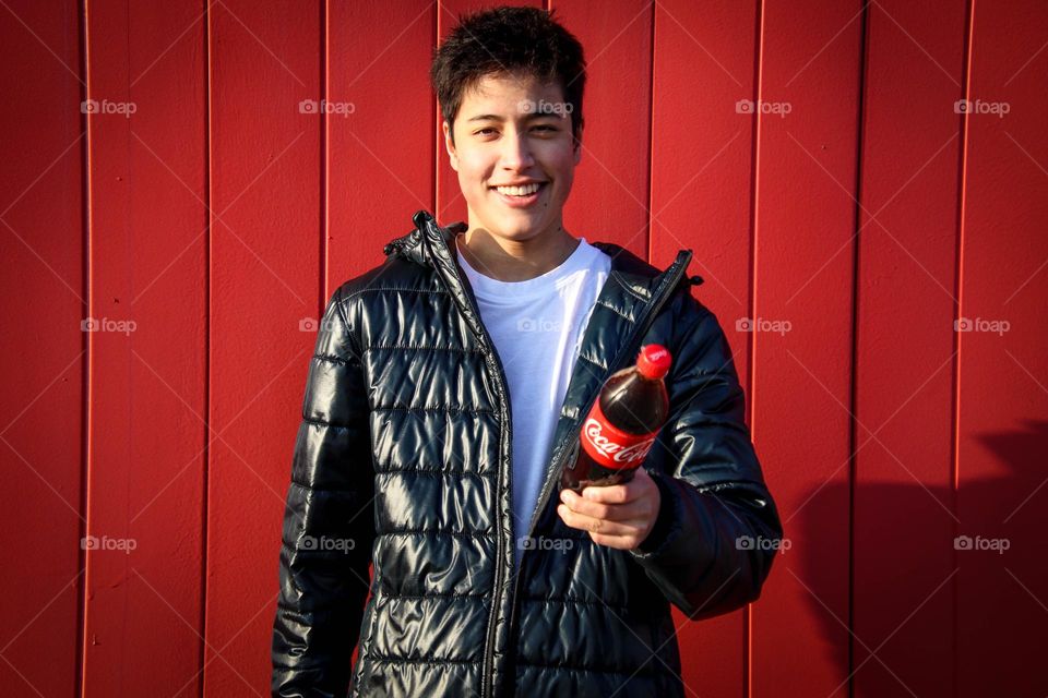 Happy teen with Coca-Cola bottle on red background