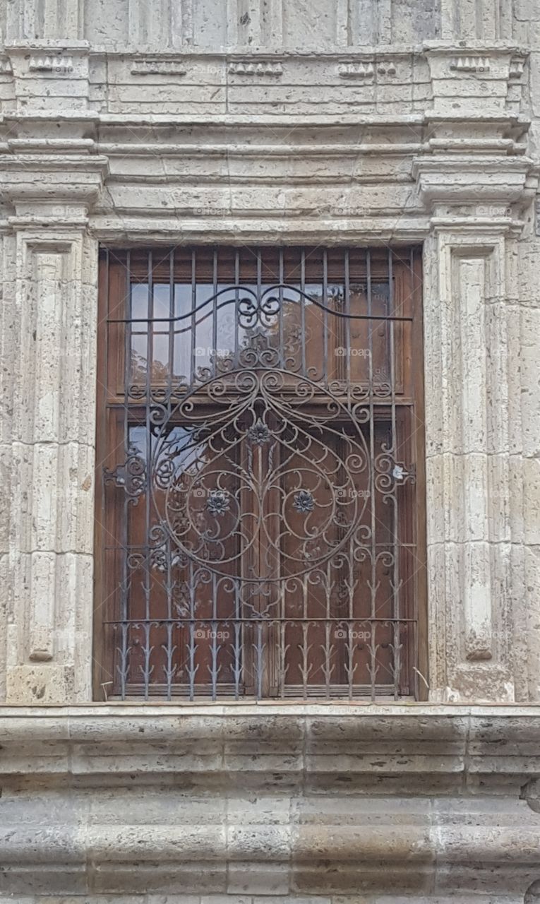 a window of many to an old government building in downtown Guadalajara. The windows are have wooden shutters on inside and outside have this beautiful iron scroll work.