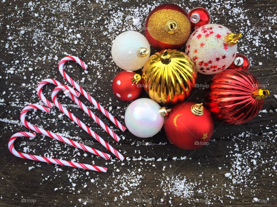 Candy canes and red and white glittering Christmas globes on rustic wooden table powdered with snow