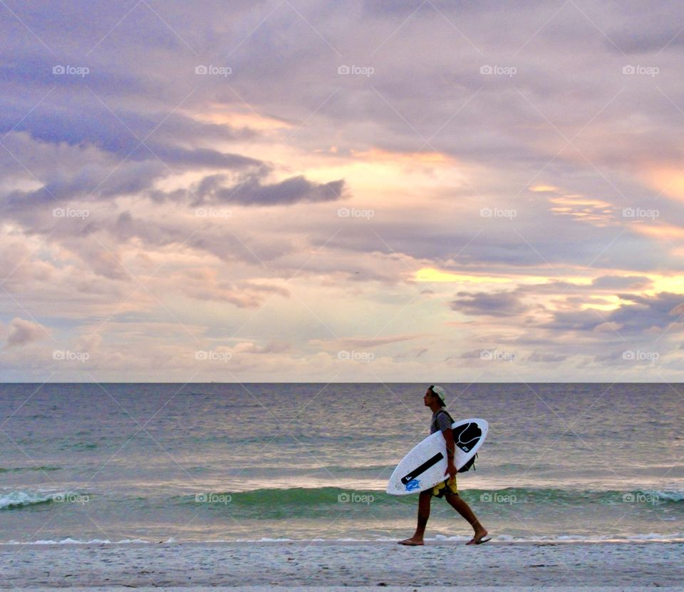 Surfer carrying his surf board on the beach 