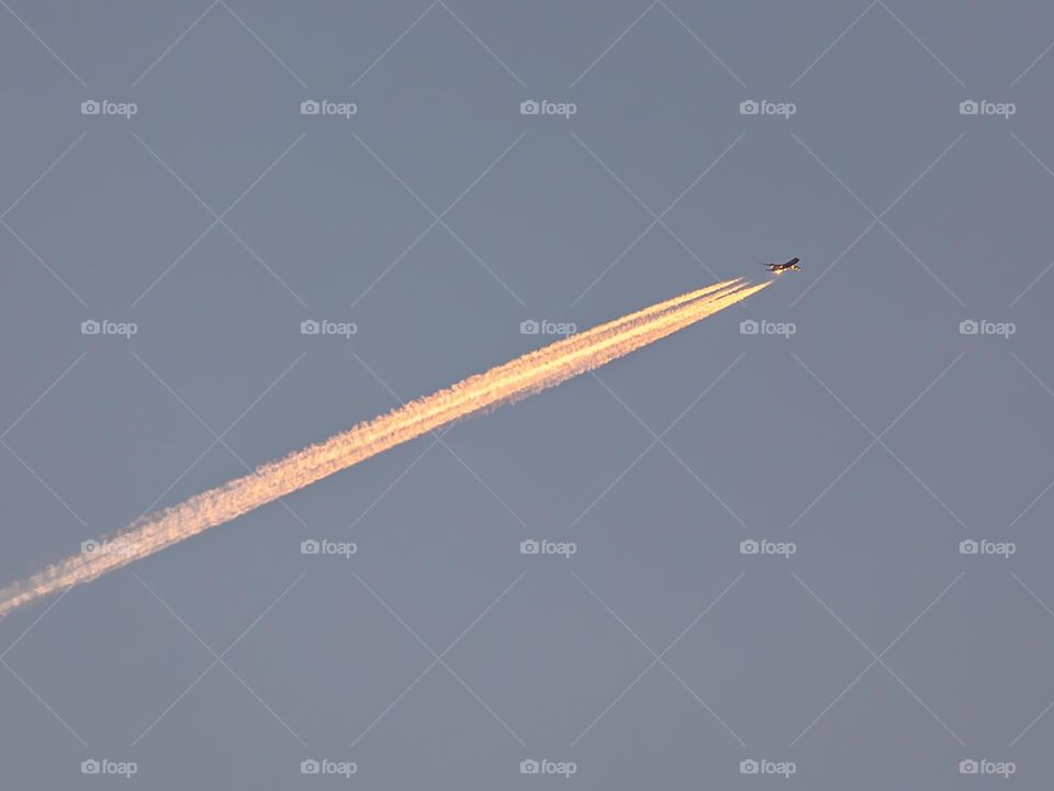 An airplane flying at dawn with a trail of engines