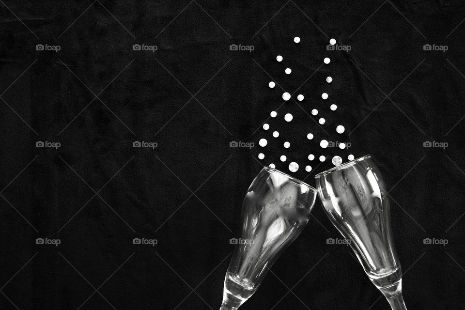 Flat lay of champagne glasses and  rhinestone bubbles on black background in black and white