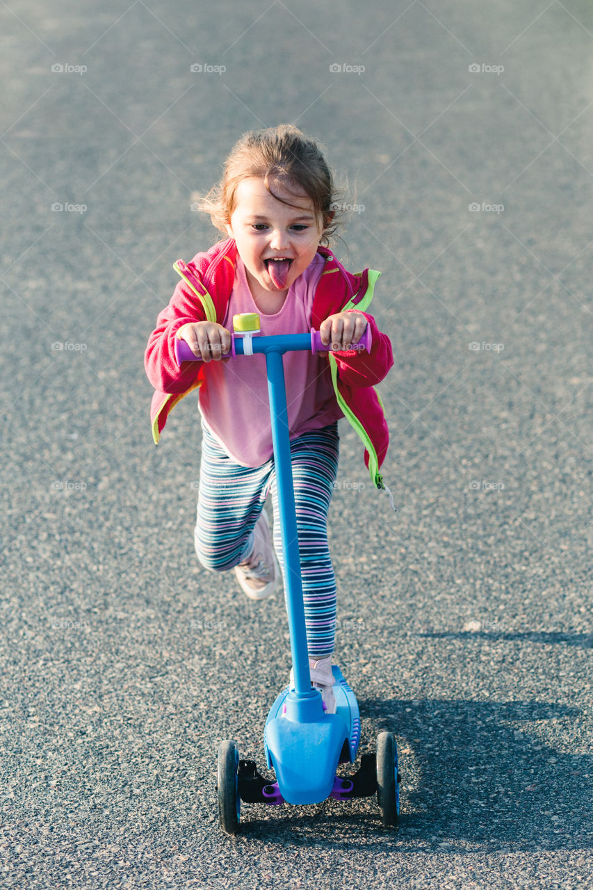 Little adorable girl having fun riding on scooter, playing outdoors. Real people, authentic situations