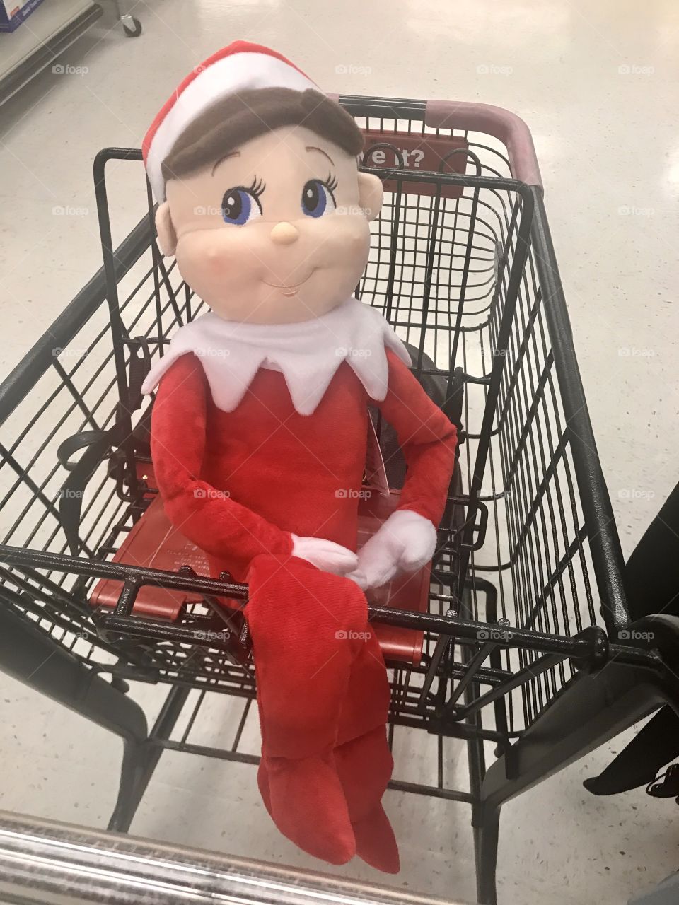 A big mischievous elf on the shelf doll wearing s red and white Christmas suit sitting in the shopping cart at the department store. USA, America 